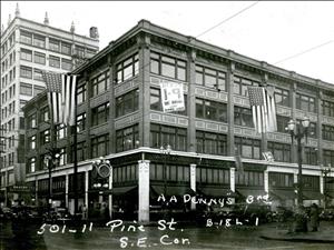 A four story brick building on the corner of a city street. American flags hang off of the building. A taller building is in the background. White ink handwriting on the image says A A denny's third five zero one pine street south east corner. 